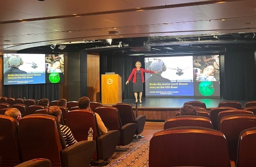Una mujer dando una conferencia en el escenario, con una presentación de PowerPoint a sus espaldas